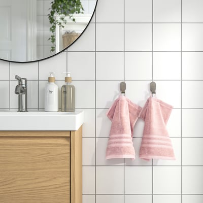 Pink towels hang on hooks near sink with soap dispensers, reflective mirror above.