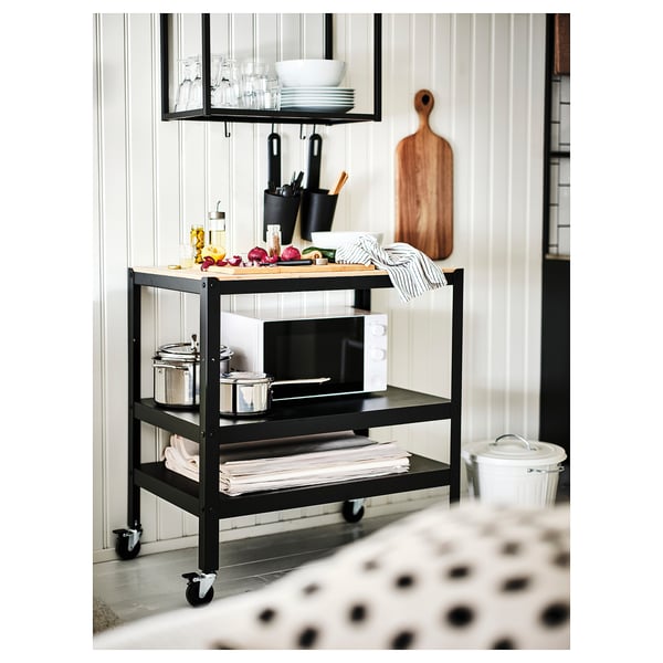 Black three-tier cart with wheels, holding kitchen items on white walls.