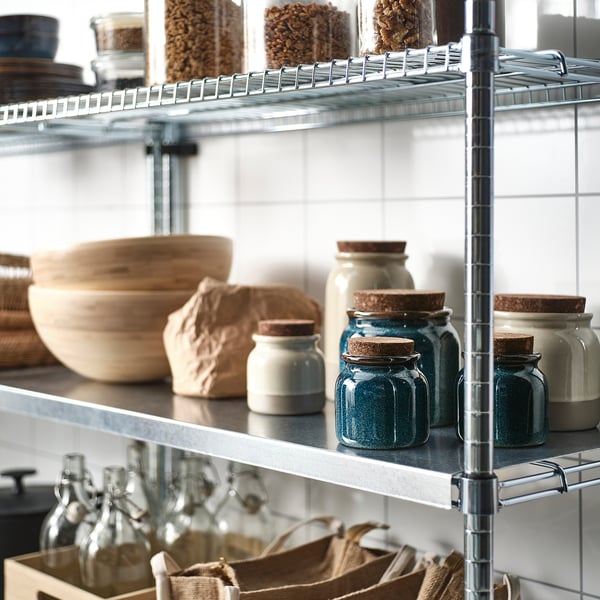 Metal shelving unit in kitchen with jars, bowls, and bottles, storing dry foods and organised neatly.