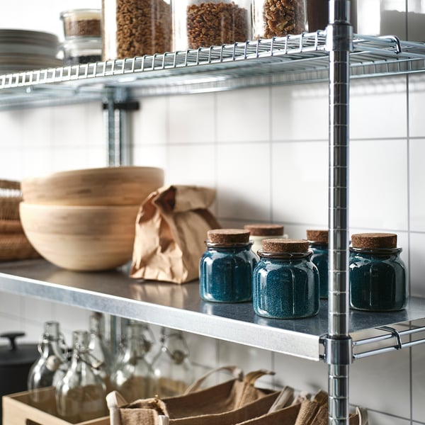 Metal kitchen shelves storing glass jars with cork lids and wooden bowls.