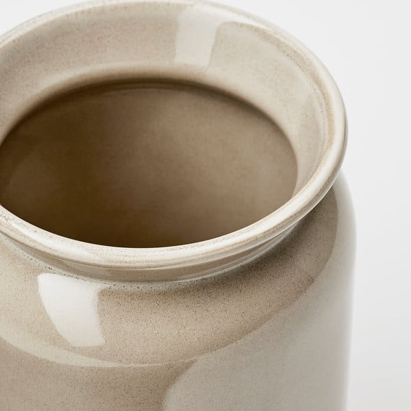 Close-up of a stoneware utensil holder. Smooth, glazed finish, neutral colour. Round opening, sides curve inward.