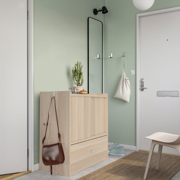 Wooden BRUKSVARA storage unit with drawers, shelves, and hanging purse, near door with shoe rack and bench.