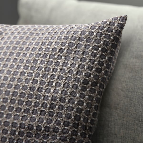 Geometric patterned cushion cover, woven with textured cotton, shown resting on a sofa.