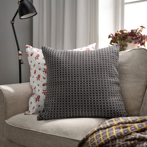 BRUNNYCKLAR grey cushion on beige couch, larger than red floral pillow, yellow checkered blanket.