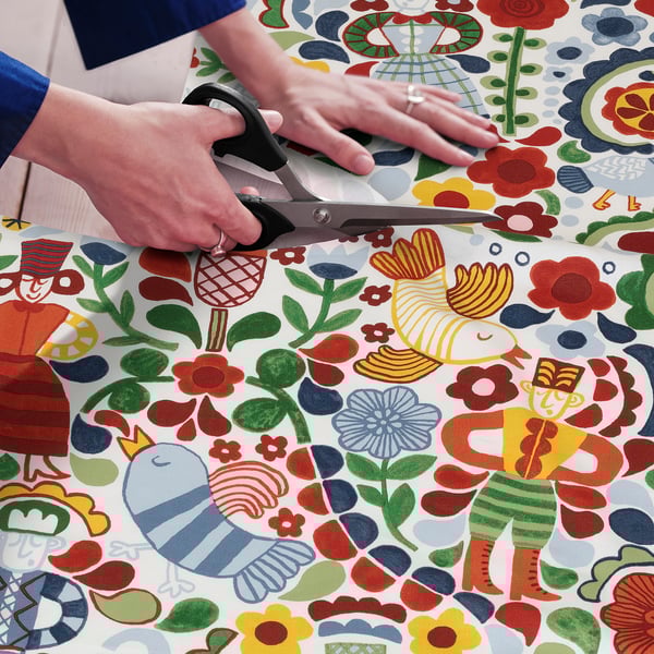Person cuts colourful, patterned fabric with scissors. The fabric folk art designs, suitable for sewing projects.