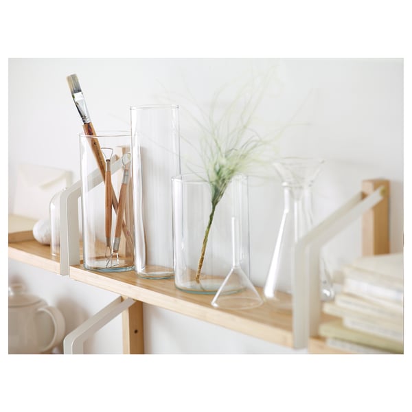 Three glass vases in varying sizes on wooden shelf. One with brush, one with plant, one empty.