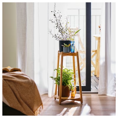 Wooden plant stand with three tiers holding vases and plants, positioned by a window.