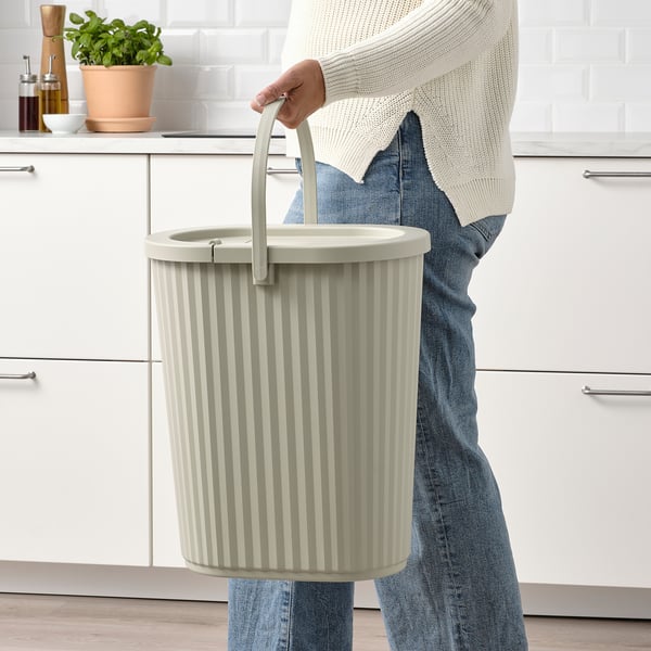 Person holding DAMMÄNG bin with handle, ideal for recycling glass, plastic, and paper, with a lid for hiding waste, standing in a modern kitchen.