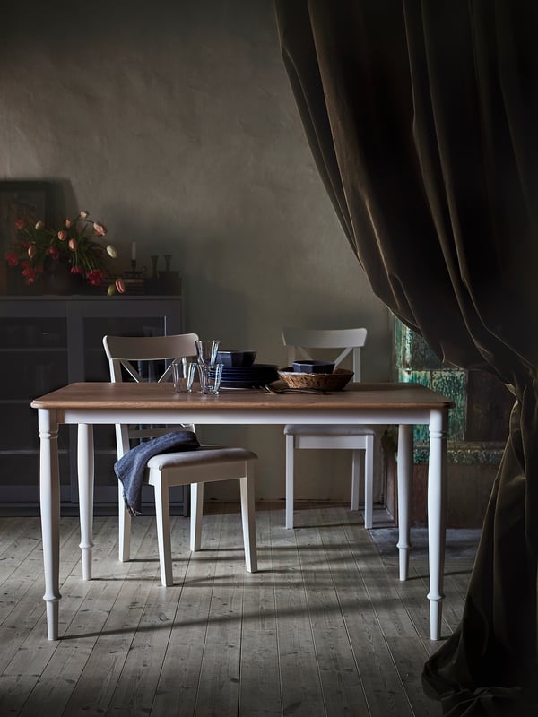 A DANDERYD dining table, white with oak veneer top, rectangular, surrounded by four matching chairs, set for dining with tableware.