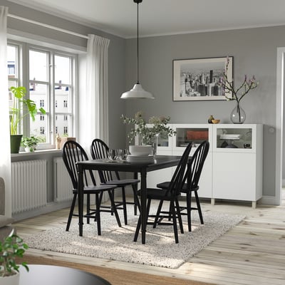 Cosy dining room with black chairs around a square table, white curtains, and a large window. A grey rug and sideboard with vases and decor.