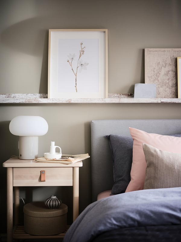 Modern bedroom with DEJSA lamp on nightstand, gray headboard, pink pillows, floral print