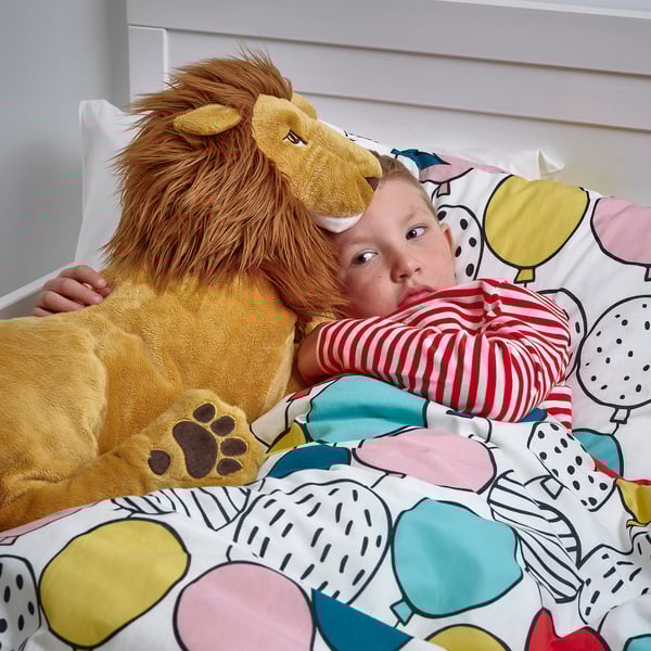 Child hugging large stuffed lion toy on bed with colourful pattern.