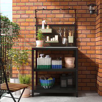 Shelf with baskets, plants & tools against brick wall.