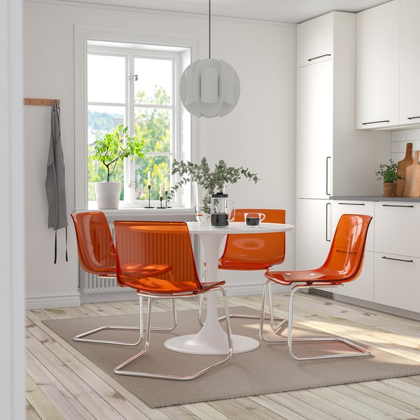 Modern kitchen with white DOCKSTA table, orange chairs, large window, and hanging light.