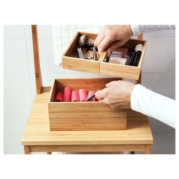 Person organises makeup in wooden boxes on a wooden table. One box holds lipsticks, the other makeup brushes.