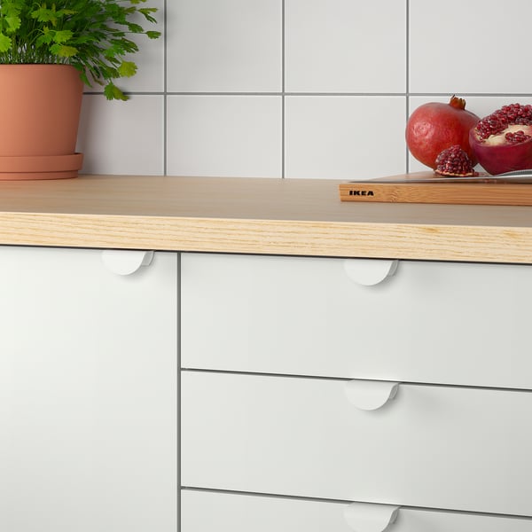 A modern kitchen counter with white drawers featuring DRAGSMARK clip-on handles, a wooden countertop, pomegranates, and a plant.