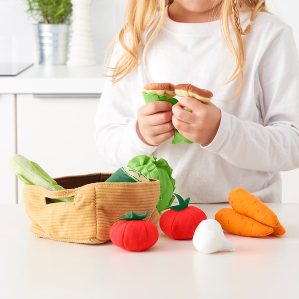 Kid plays with toy veggies and burger near basket.