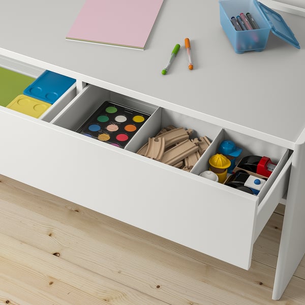 White kids activity table with open drawers filled with toys and art supplies. The table has compartments for storing items.
