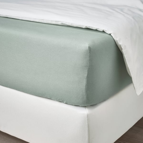 A fitted grey-green bed sheet made of cotton, shown on a white mattress. Its designed to fit mattresses up to 26 cm thick with elastic edging.