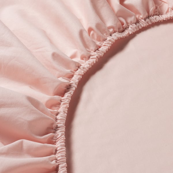 Close-up of soft, pink fitted sheet with elastic edges, showcasing its smooth cotton texture and craftsmanship.