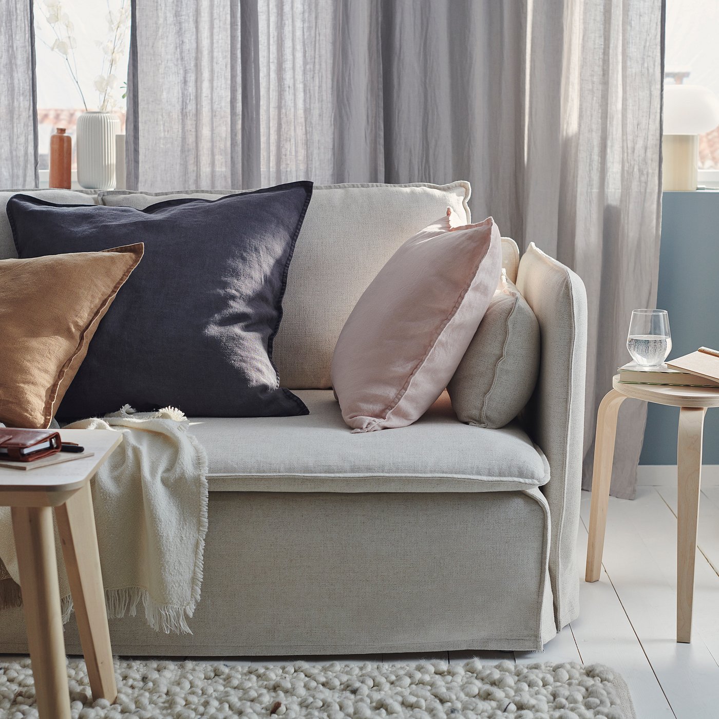 A cosy grey sofa with multiple cushions and blankets. Soft textiles, varied textures, and warm decor create a welcoming living space.