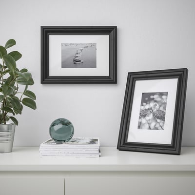 Two picture frames on shelf with plant, one with boat, one with butterfly.