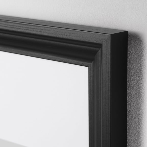 Black picture frame with smooth, robust design on wall, soft profile, and plastic protection.