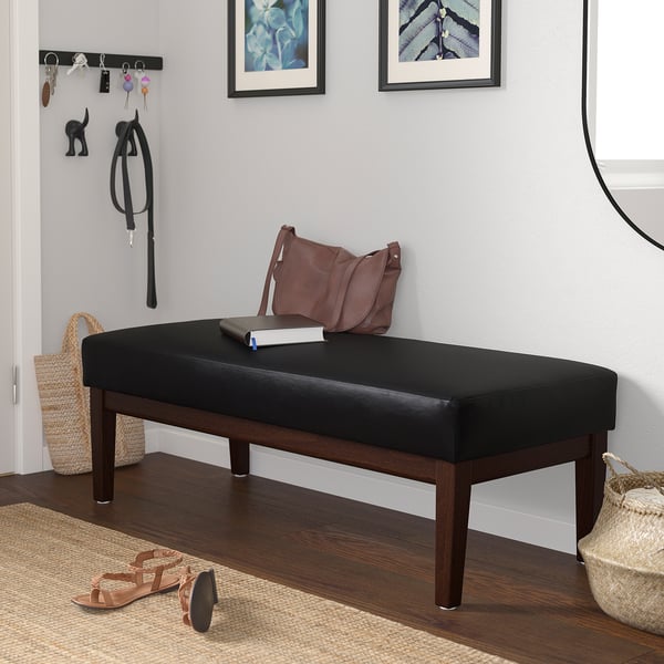 Black bench with brown handles against wall, near coat & sandals.