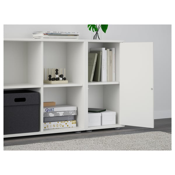 White EKET storage unit with shelves holding various items, including decorative objects, games, and books. Closed storage with a push-opener door.