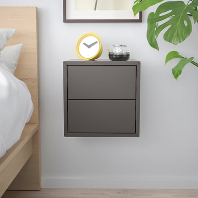 Minimalist bedroom with dark grey EKET cabinet, plant, and clock.