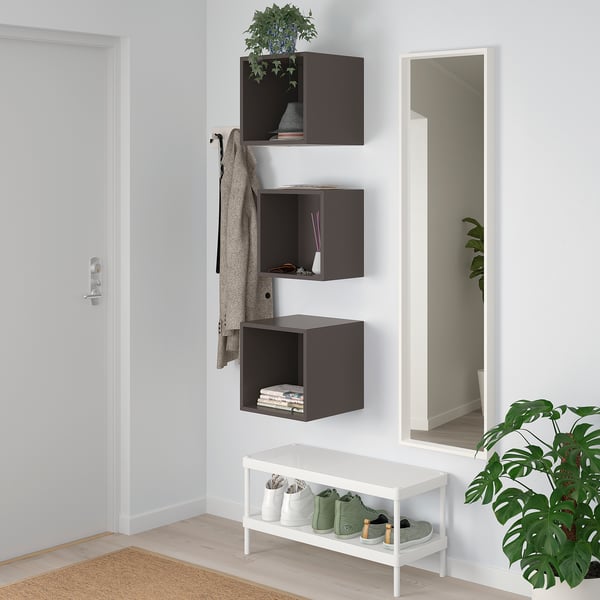 Dark grey EKET cubes with plant, books, drawer; white bench with shoe rack, mirror, coat hook, jacket, and green plant.