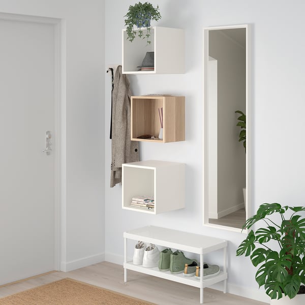 Small EKET shelves on wall, white & wood, storing books & decor, with large mirror beside, under a clothes hook.