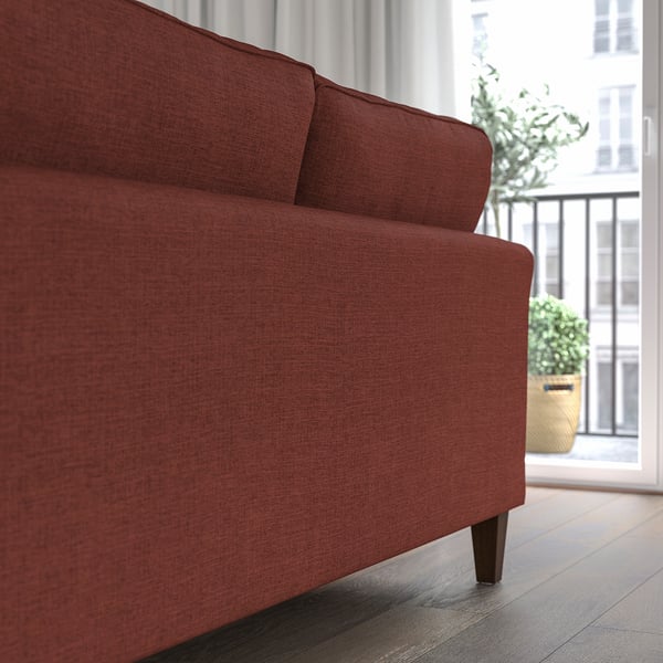 A modern red sofa with wooden legs, positioned near a large window, offering comfort with its pocket springs and removable, washable cover.