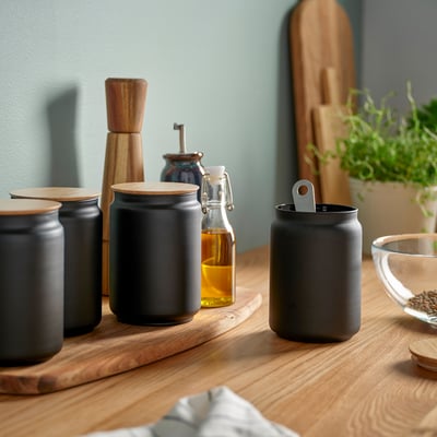 Modern kitchen display with black ceramic canisters, wood accents, and glass bottles on wooden shelf.