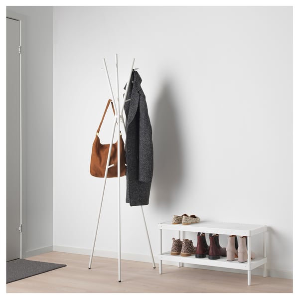 White EKRAR coat stand with hooks holds a brown bag and grey sweater; next to it, a white shoe rack with boots.