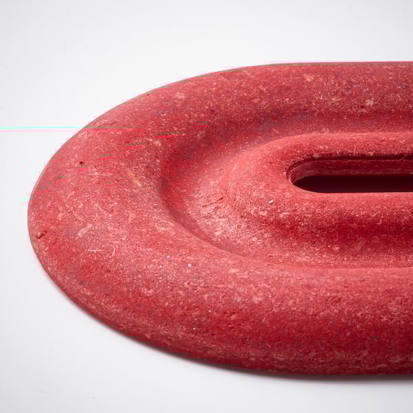 Red speckled trivet made of compressed bamboo, designed to protect surfaces from heat, showcasing a textured, vibrant finish.