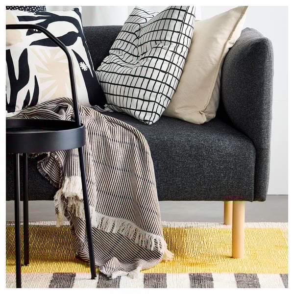 A modern grey sofa with yellow and black striped rug, featuring patterned pillows and a striped blanket.
