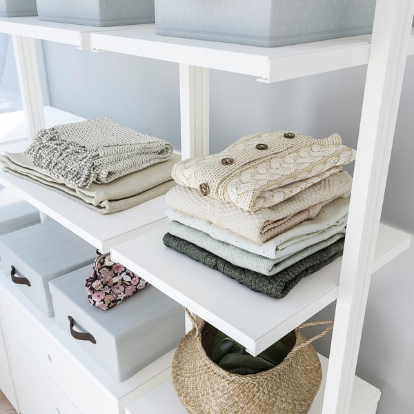 White ELVARLI shelves with neatly folded clothes and woven baskets, utilising vertical space from floor to ceiling.