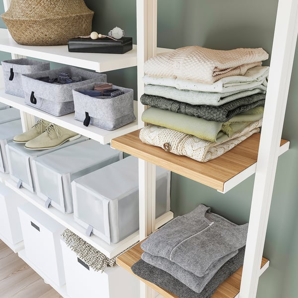 Organised closet with shelves, storage bins, and folded clothes; white frame with bamboo shelf.