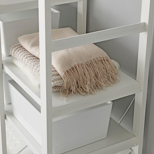 White storage unit with shelves, holding neatly folded blankets and white storage boxes.