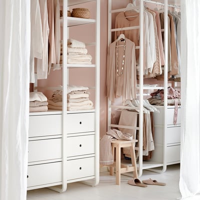 Neatly organised closet with light-colored clothes on white shelves and drawers. Hanging rail and decorative items.
