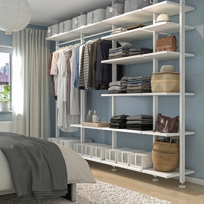 Bedroom with ELVARLI shelves storing clothes and accessories, light walls, grey curtains.