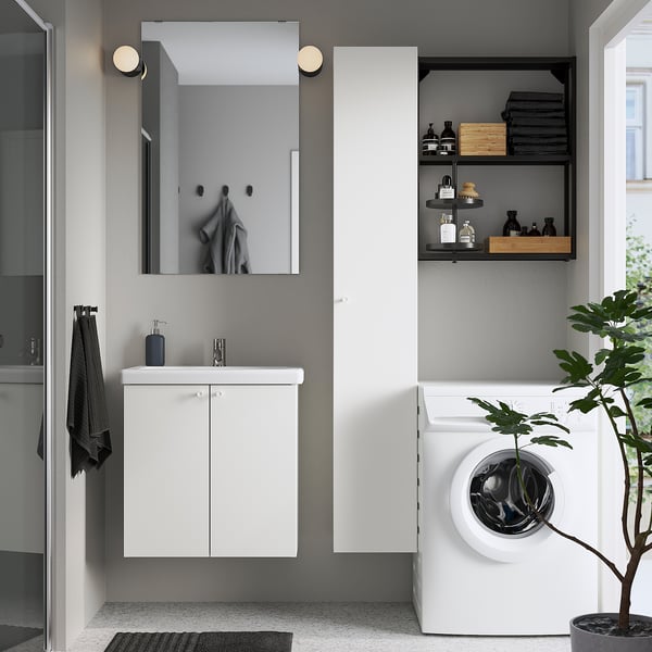 A modern bathroom with ENHET vanity, mirror, open shelves, and washing machine. Grey walls, a black towel, and plant.