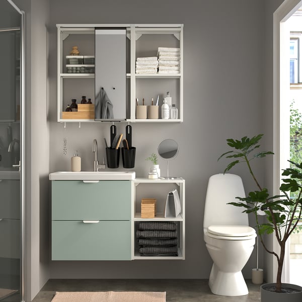Modern bathroom with blue cabinet, mirror, toilet, and plant.