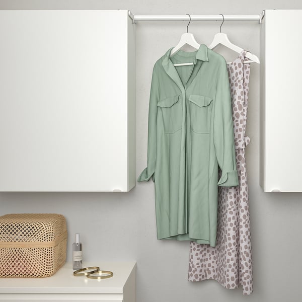 An extendable clothes rail hangs between cabinets, holding a green shirt and spotted dress, demonstrating its space-saving functionality.