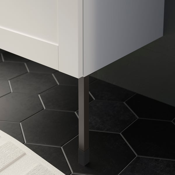 White bathroom unit on black hexagonal floor tiles, supported by adjustable black legs.