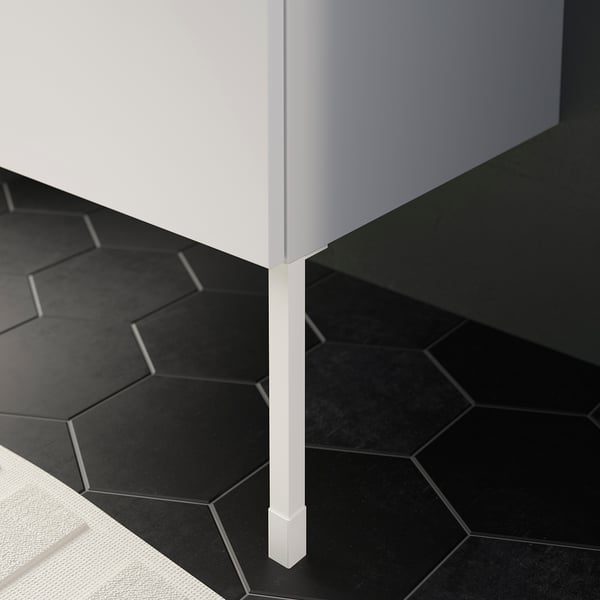 White ENHET cabinet leg standing on dark tiles, providing stability and height adjustment.