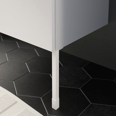 White ENHET cabinet leg standing on dark tiles, providing stability and height adjustment.