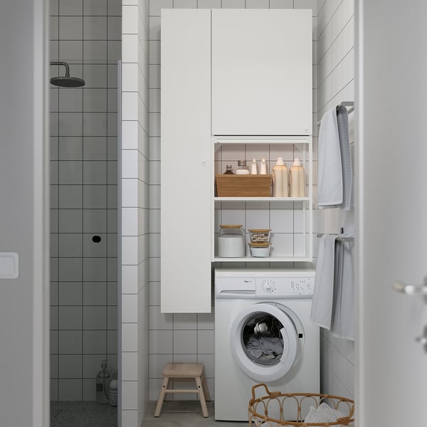 Modern bathroom with ENHET white storage cabinet, washing machine, hanging towels, wooden stool, and wicker laundry basket, next to shower.