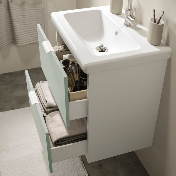 Modern bathroom vanity with open drawer showing makeup brushes and towels, ceramic sink, and towel holder.